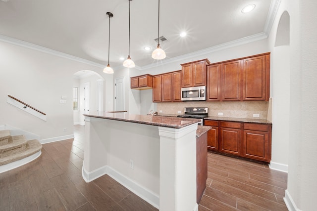 kitchen featuring dark stone counters, dark wood finished floors, arched walkways, appliances with stainless steel finishes, and brown cabinets