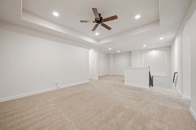 spare room with a raised ceiling, arched walkways, light colored carpet, and recessed lighting