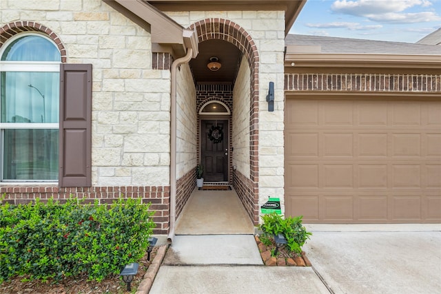 view of exterior entry with an attached garage, concrete driveway, and stone siding