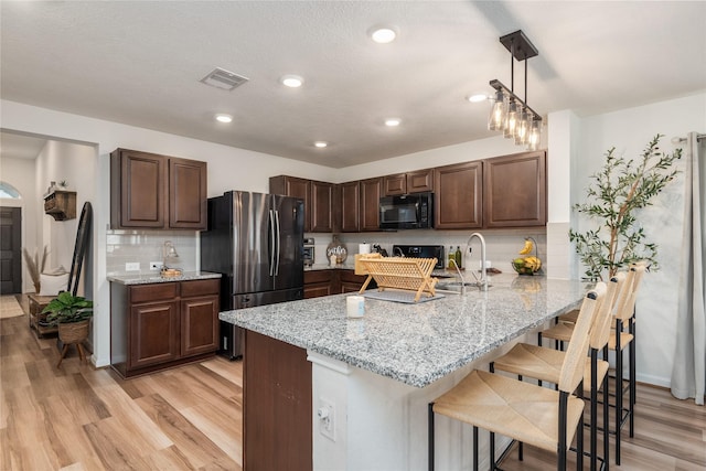 kitchen with black microwave, a sink, freestanding refrigerator, a peninsula, and light wood-style flooring