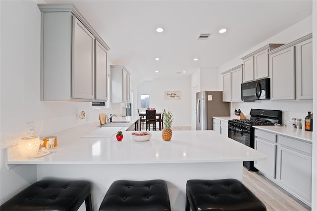 kitchen featuring a kitchen breakfast bar, gray cabinets, a peninsula, visible vents, and black appliances