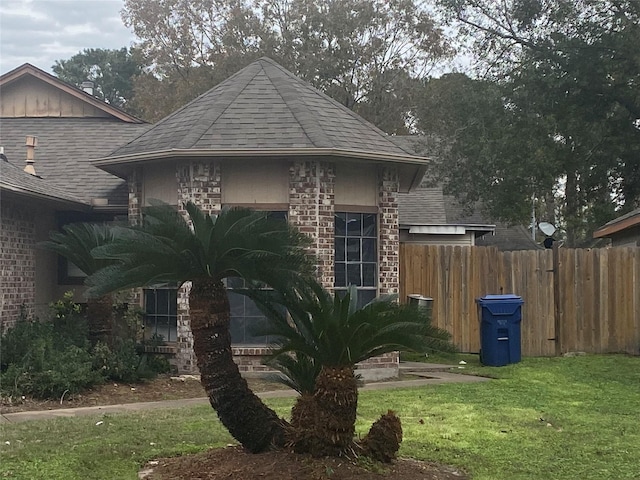 view of front of property with a front yard, fence, brick siding, and a shingled roof