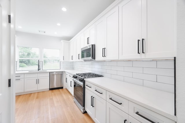 kitchen with white cabinets, light wood finished floors, visible vents, a sink, and appliances with stainless steel finishes
