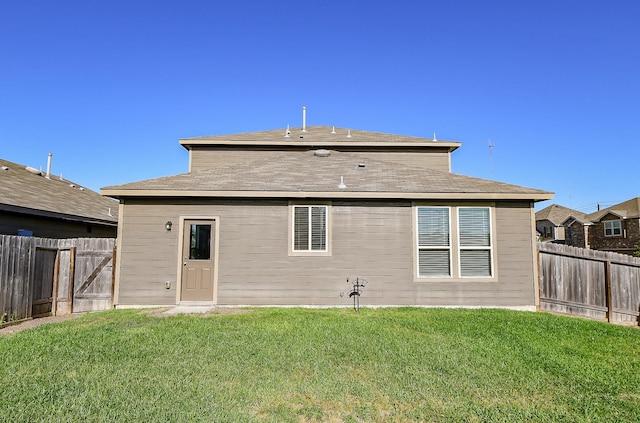 rear view of property featuring a shingled roof, a fenced backyard, and a lawn