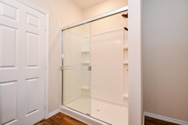 full bath featuring baseboards, tiled shower, and wood finished floors