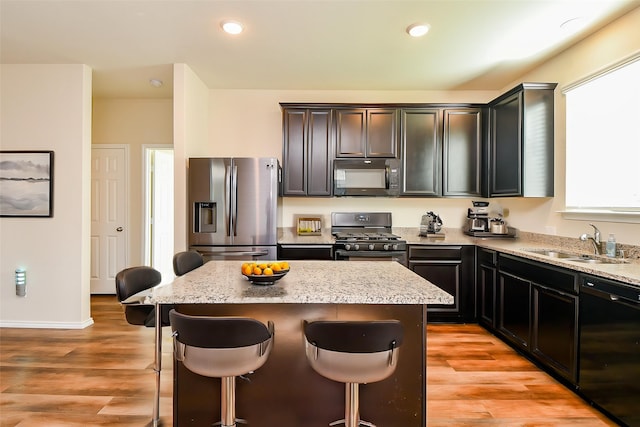 kitchen featuring a center island, a sink, black appliances, light stone countertops, and a breakfast bar area