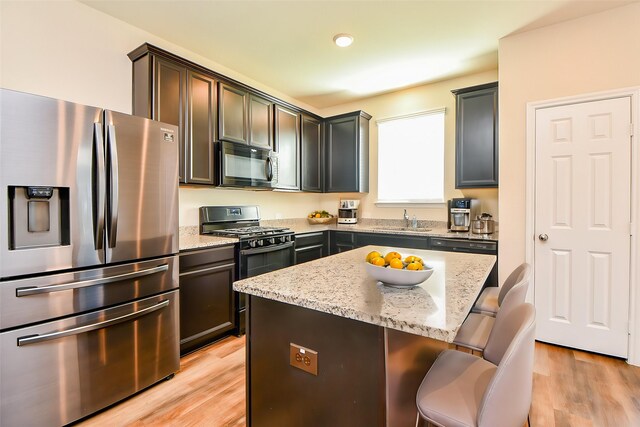 kitchen featuring light stone countertops, a kitchen bar, light wood-type flooring, black appliances, and a sink