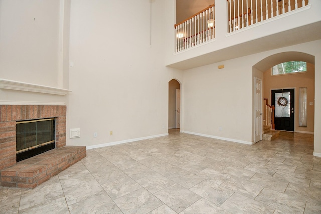 unfurnished living room featuring arched walkways, a high ceiling, marble finish floor, and baseboards