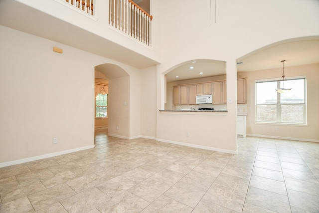 unfurnished living room featuring arched walkways, a towering ceiling, and baseboards
