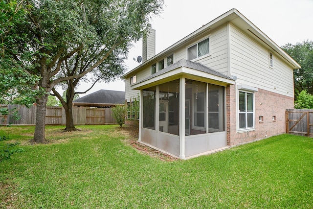 rear view of property with a sunroom, a lawn, a chimney, a fenced backyard, and brick siding