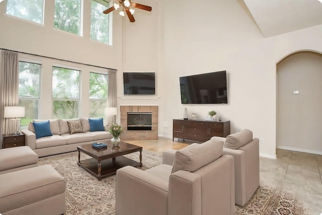 living room featuring a tile fireplace, a towering ceiling, arched walkways, baseboards, and ceiling fan