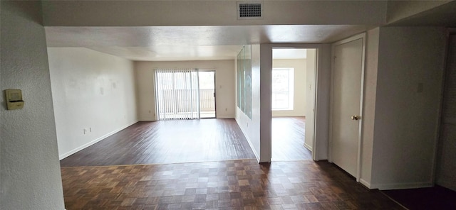 empty room with visible vents, baseboards, parquet floors, and a textured wall