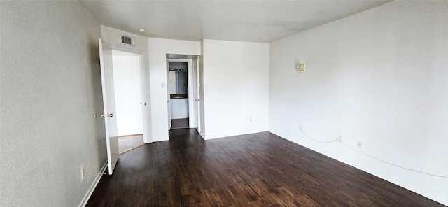 empty room featuring baseboards, dark wood-style floors, and visible vents