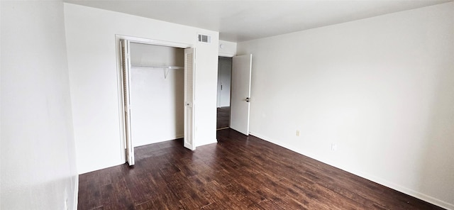 unfurnished bedroom featuring dark wood-type flooring, a closet, baseboards, and visible vents
