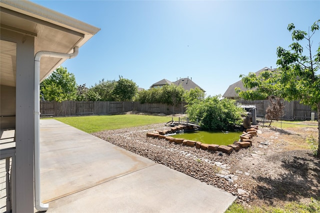 view of yard featuring a patio area, a fenced backyard, and a garden pond