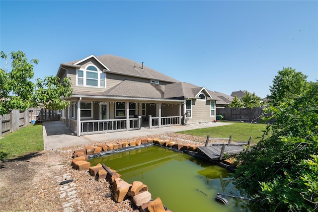 rear view of property with a lawn, a patio area, a small pond, and a fenced backyard
