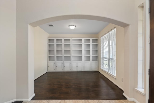 spare room with arched walkways, dark wood finished floors, and visible vents