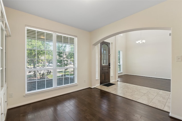 foyer entrance featuring baseboards, arched walkways, a notable chandelier, and hardwood / wood-style flooring