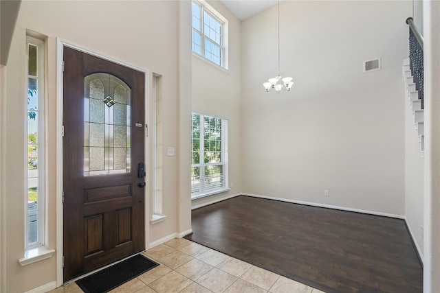 tiled entrance foyer featuring a towering ceiling, a notable chandelier, visible vents, and a wealth of natural light