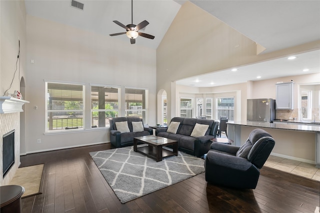 living room featuring high vaulted ceiling, arched walkways, a ceiling fan, visible vents, and a tile fireplace