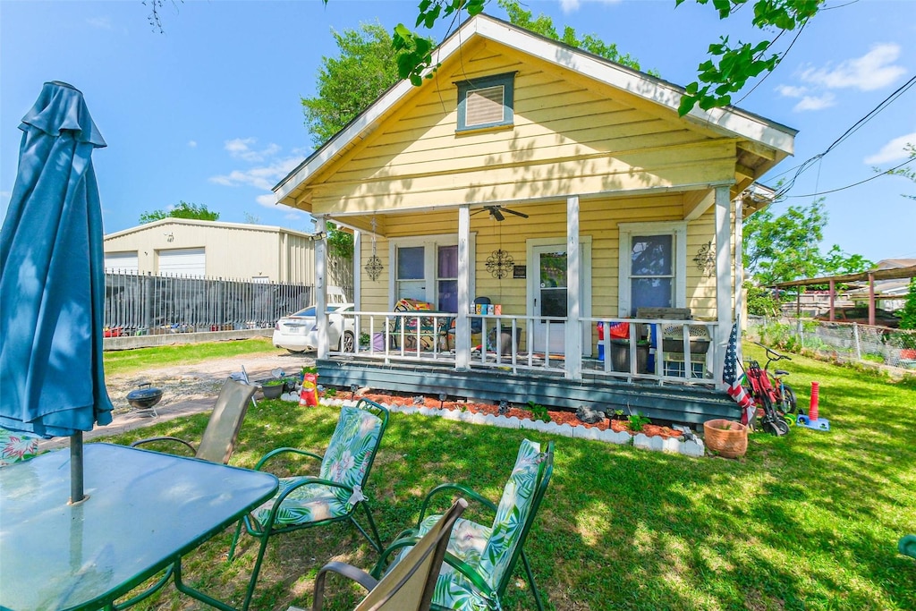 rear view of house with covered porch, ceiling fan, fence, and a lawn
