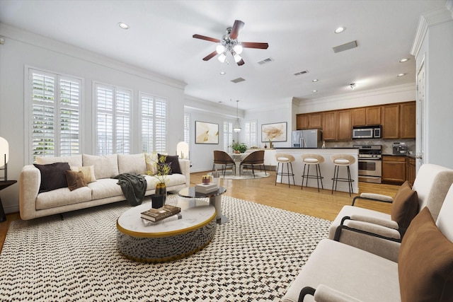 living room with ornamental molding, a ceiling fan, visible vents, and light wood-style floors