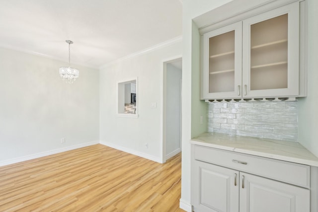 7463 Brompton St Unit 7463, Houston, TX 77025 - kitchen with backsplash, ornamental molding, light wood-style flooring, glass insert cabinets, and hanging light fixtures