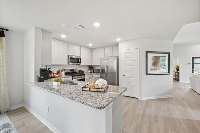 kitchen with visible vents, appliances with stainless steel finishes, a peninsula, light wood finished floors, and light stone countertops