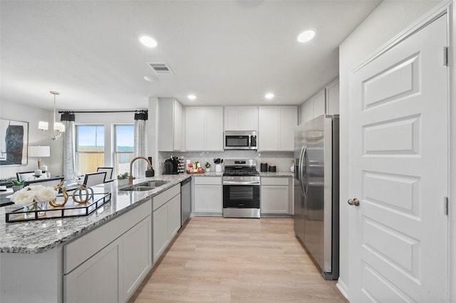 kitchen with light wood-type flooring, light stone counters, visible vents, stainless steel appliances, and a sink