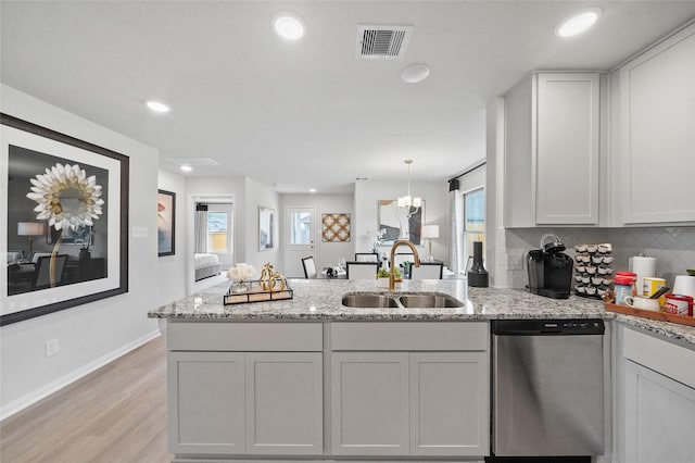 kitchen with baseboards, a peninsula, visible vents, stainless steel dishwasher, and a sink
