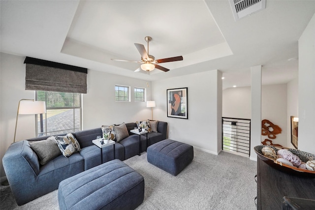 living room featuring carpet flooring, visible vents, a tray ceiling, and a ceiling fan
