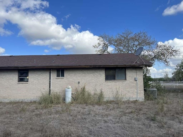 view of home's exterior featuring central air condition unit, a shingled roof, fence, and brick siding