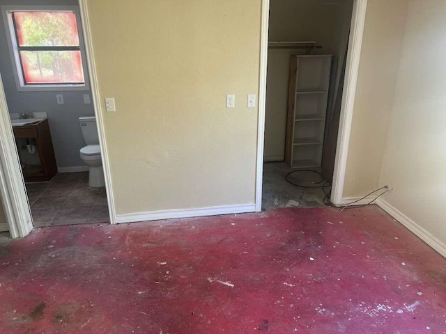 unfurnished bedroom featuring a sink, ensuite bathroom, and baseboards