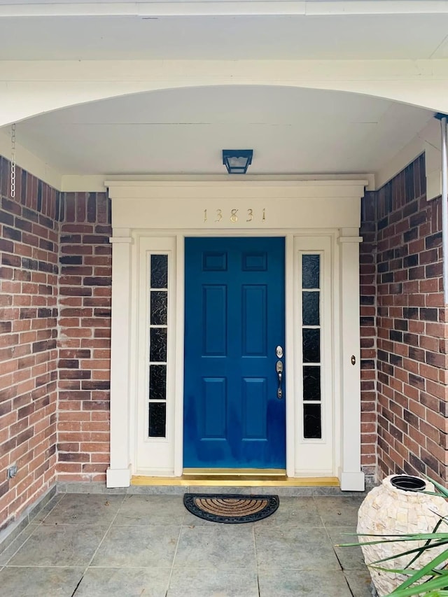 doorway to property featuring a porch and brick siding