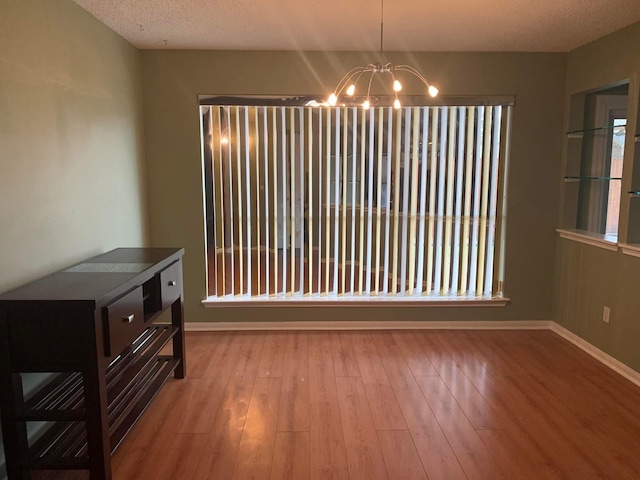unfurnished dining area with a chandelier, wood finished floors, and baseboards