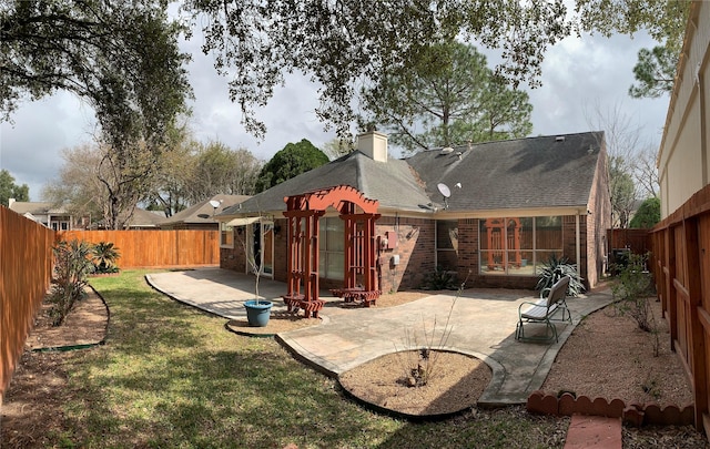 back of house featuring a patio, a chimney, a fenced backyard, and brick siding