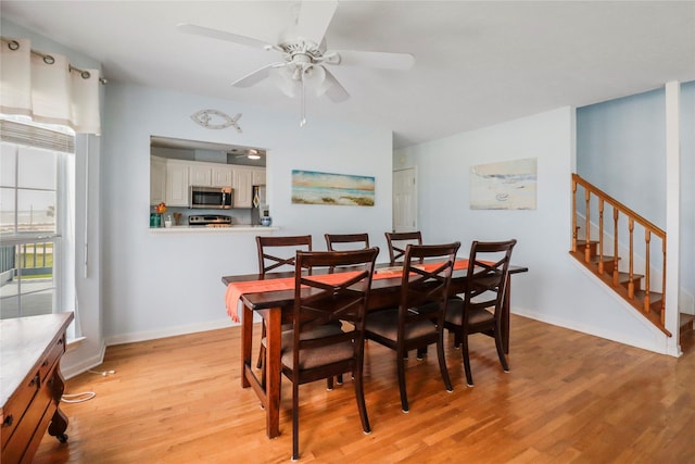 dining space with baseboards, light wood-style flooring, ceiling fan, and stairs