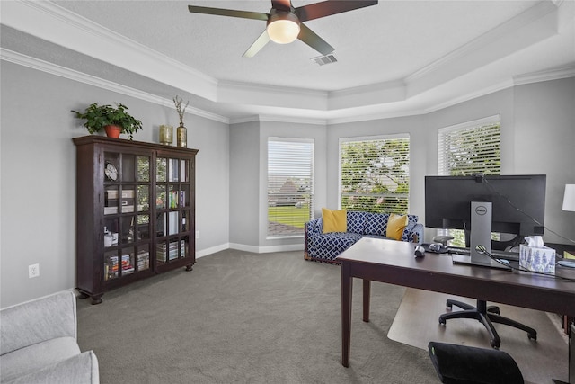 carpeted office with visible vents, baseboards, ornamental molding, a ceiling fan, and a tray ceiling
