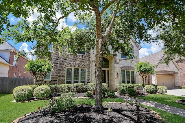 view of front of house with driveway, stone siding, brick siding, an attached garage, and fence