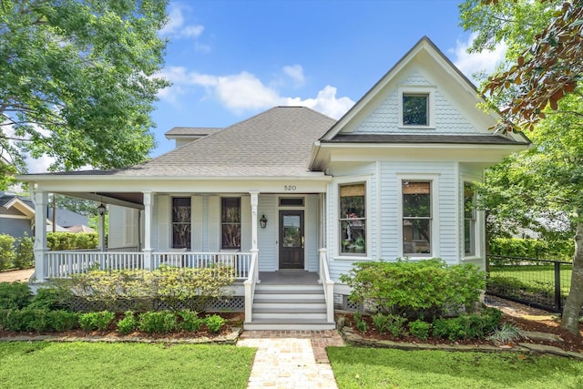 view of front of house featuring covered porch, fence, a shingled roof, and a front yard