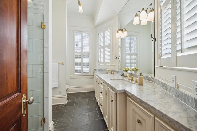 bathroom featuring stone tile flooring, double vanity, toilet, baseboards, and a sink