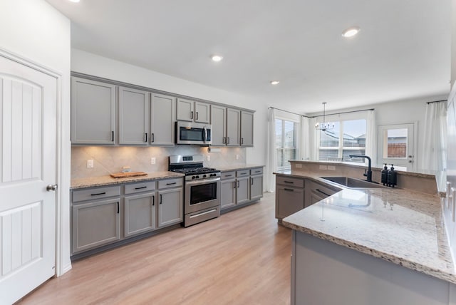 23830 Via Leoni Dr, New Caney, TX 77357 - kitchen with stainless steel appliances, gray cabinets, a sink, light wood-style flooring, and decorative backsplash