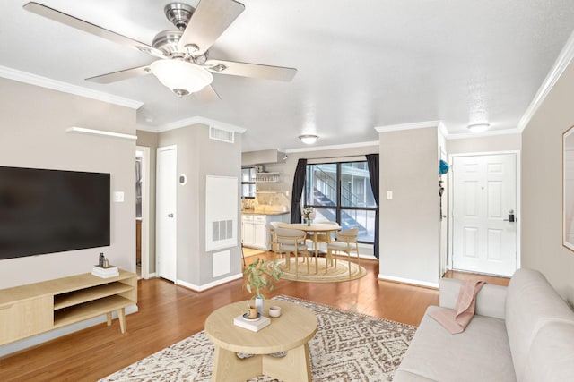 living room with visible vents, a ceiling fan, crown molding, and wood finished floors