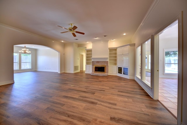 unfurnished living room featuring crown molding, ceiling fan with notable chandelier, dark wood-style flooring, and visible vents