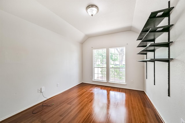 unfurnished room featuring lofted ceiling, baseboards, and wood finished floors