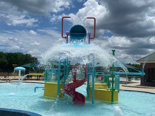 view of play area featuring fence, a water play area, and a community pool