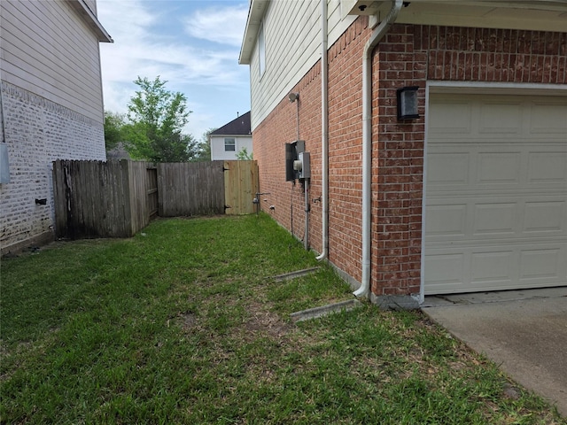 view of side of home featuring a garage, brick siding, fence, and a yard