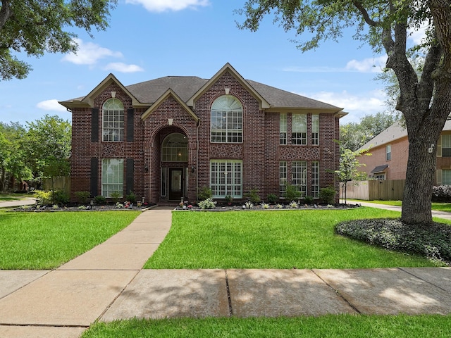 view of front facade featuring brick siding, fence, and a front yard