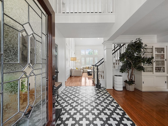 foyer entrance featuring crown molding, decorative columns, a towering ceiling, wood finished floors, and stairway