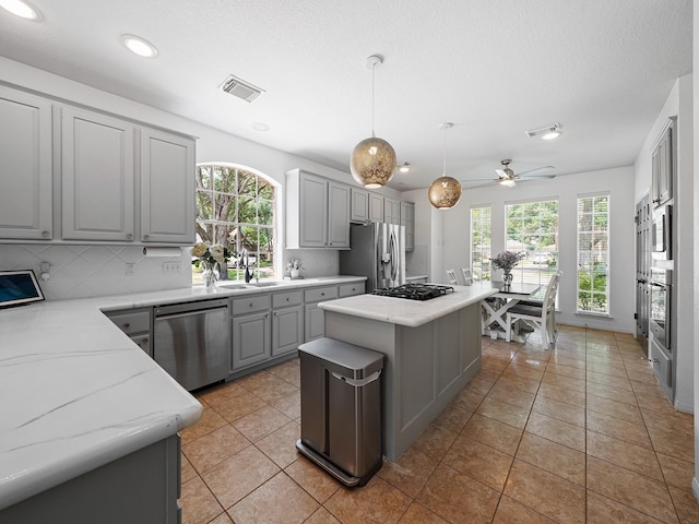 kitchen with appliances with stainless steel finishes, a sink, visible vents, a center island, and gray cabinetry